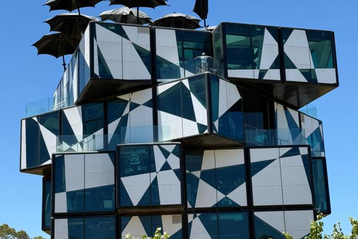 Modern geometric building with black umbrellas on roof, surrounded by greenery.