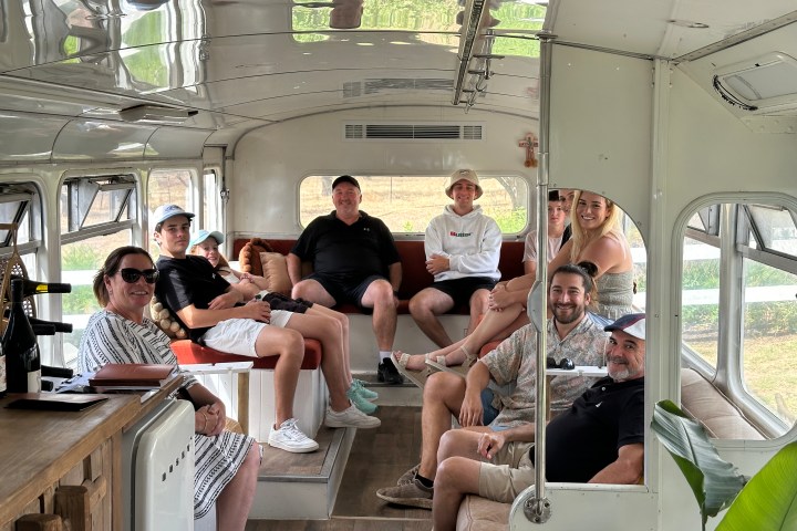Group of people sitting in a retro-style bus interior with large windows.