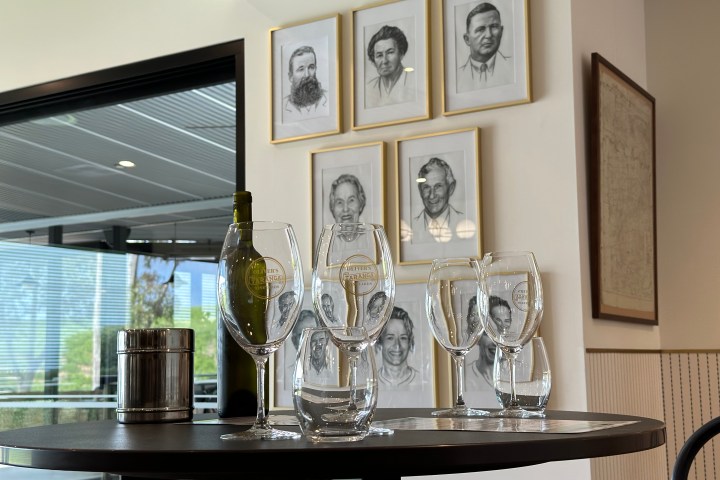 Table with wine glasses, bottle, and six portraits on a wall.
