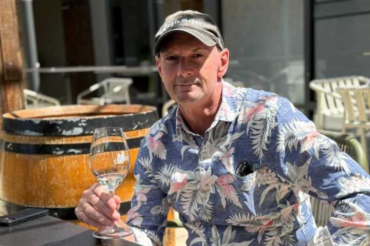 Man in floral shirt and cap holding wine glass at outdoor cafe table.
