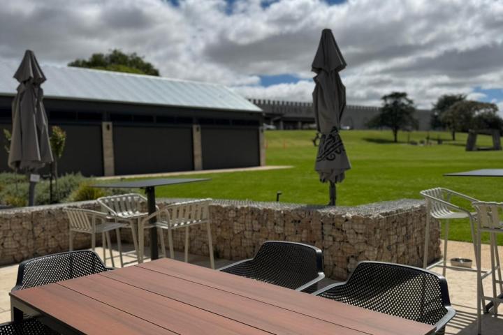 Outdoor seating with wooden table, chairs, umbrellas, and a grassy area under cloudy sky.