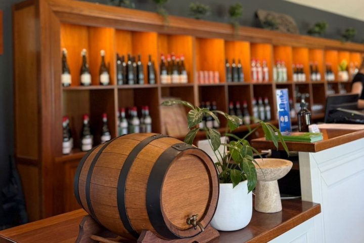 Wine shop counter with a small barrel, plants, and a wine display rack in the background.