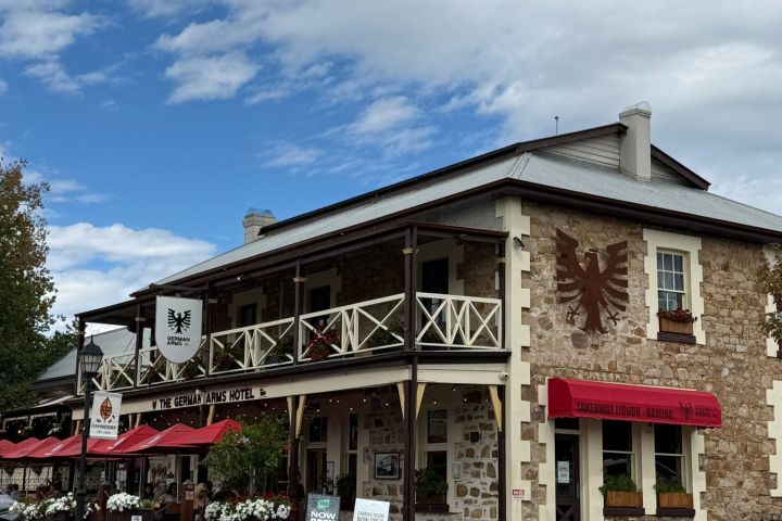 Stone building with red awnings and a sign reading 'The German Arms Hotel' on a cloudy day.