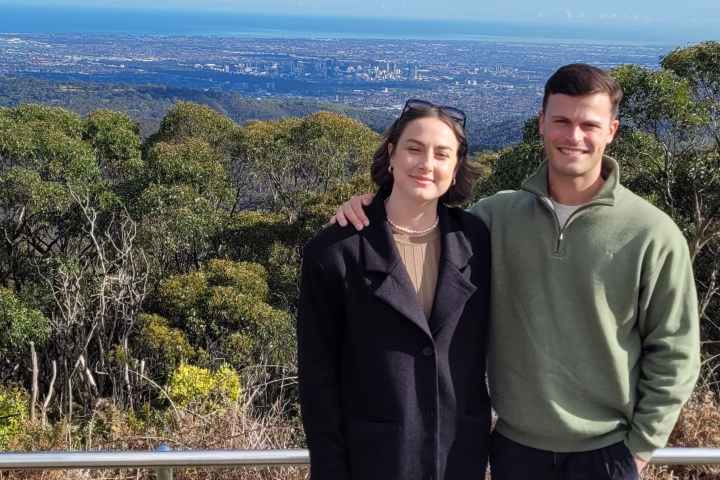 Couple posing in front of cityscape and blue sky with clouds.