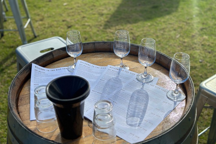 Wine tasting setup on a barrel with glasses, menus, and a spittoon outside.
