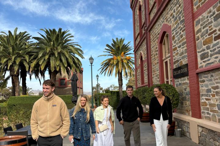 Five people walking beside a stone building with palm trees in the background on a sunny day.