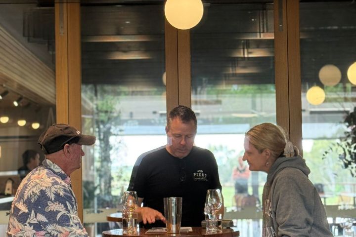 Three people sit at a bar table with drinks and chat in a modern interior.