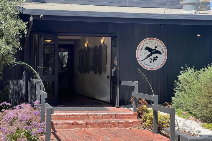 Entrance to a farm shop with a circular sign and red brick steps, surrounded by plants.