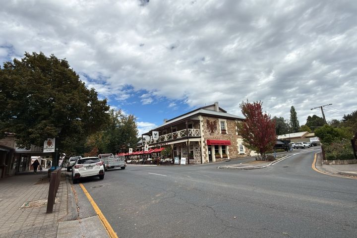 Street view with stone building, outdoor café, parked cars, and cloudy sky.