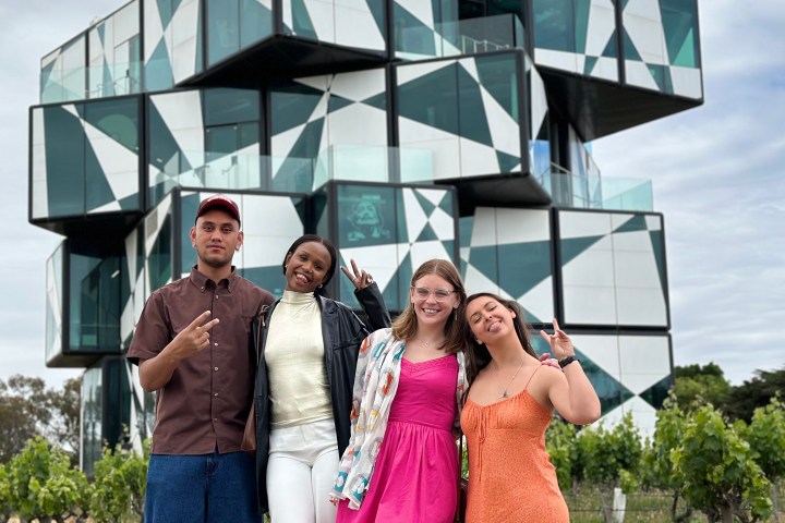 Four people standing in front of a geometric building with patterned windows.