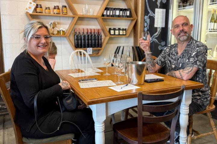 Two people sitting at a table with wine glasses in a cozy room with wooden shelving.