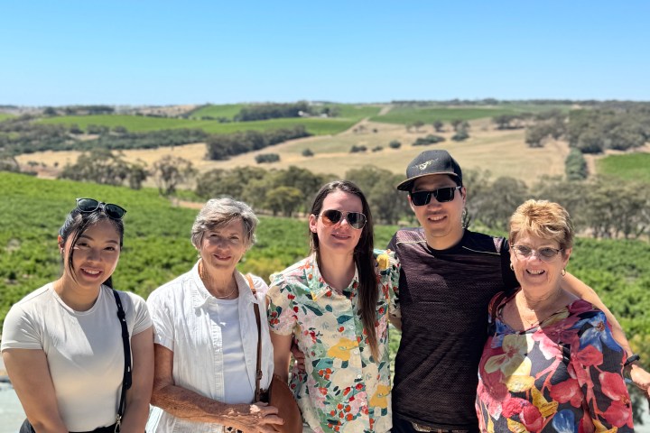 Five people standing together outside with green fields in the background and a clear blue sky.