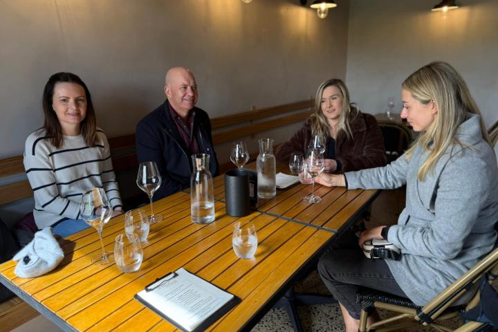 Four people sitting at a wooden table with empty glasses in a cozy room.