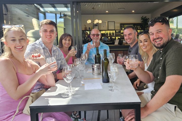 Group of people smiling and holding glasses at a table outside a restaurant.