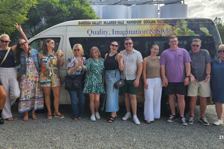 Group of people posing happily in front of a tour bus on a sunny day.
