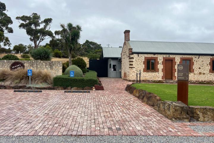 Stone building with brick path and greenery, featuring 'Olivers Taranga' sign and accessible parking signs.