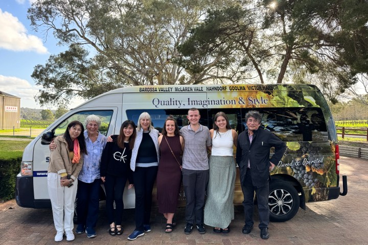 Group of eight people posing in front of a tour van with trees in the background.