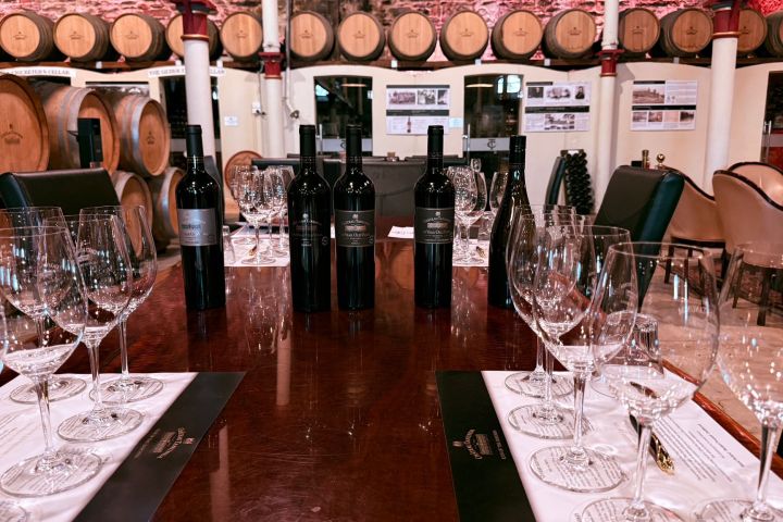 Wine tasting setup with bottles, glasses, barrels in background.