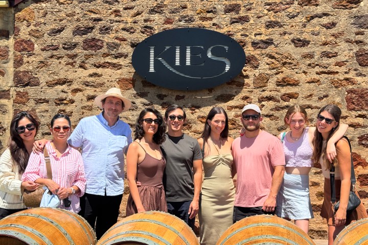 Group of friends standing in front of stone building with sign and wine barrels.