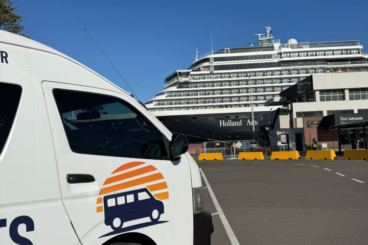 Van with sunrise logo parked near a large cruise ship at a port.