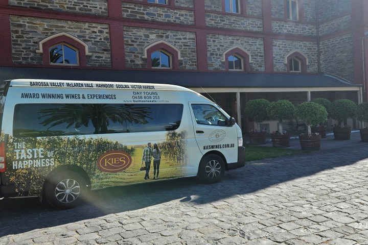 Van with vineyard graphics parked by a historic stone building under a clear blue sky.