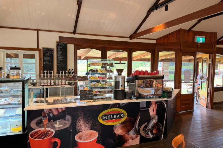 Cozy cafe interior with wooden beams, counter with coffee machines, snacks, and menu displayed.