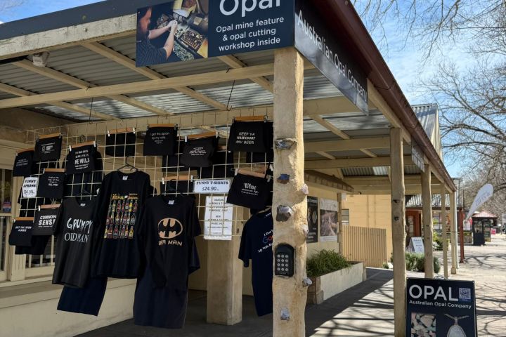 Outdoor shop with hanging T-shirts and signs advertising opals and jewelry workshops.