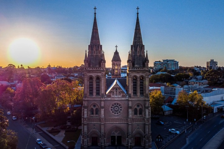 Church with twin spires at sunset, cityscape in background.