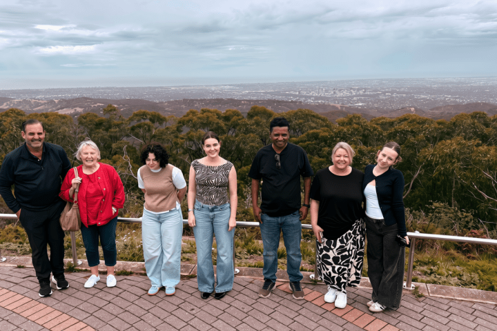 Group of seven people standing on a lookout with hills and cloudy sky in the background.