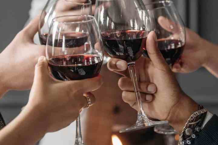 Group of people toasting with red wine glasses around a candlelit table.