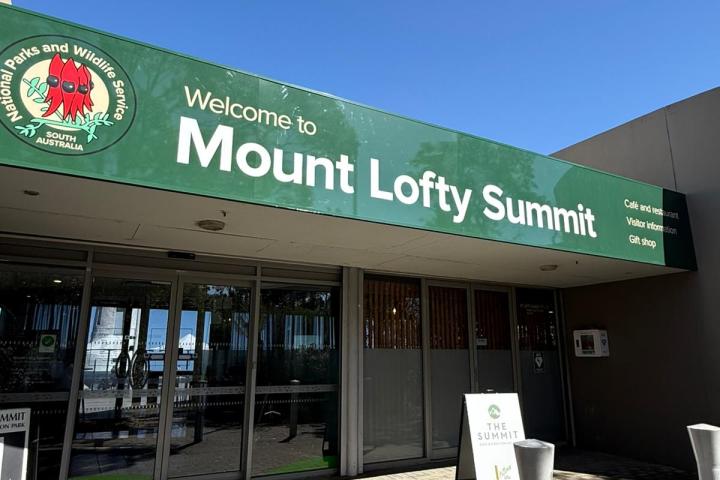 Entrance of Mount Lofty Summit with green sign under clear blue sky.