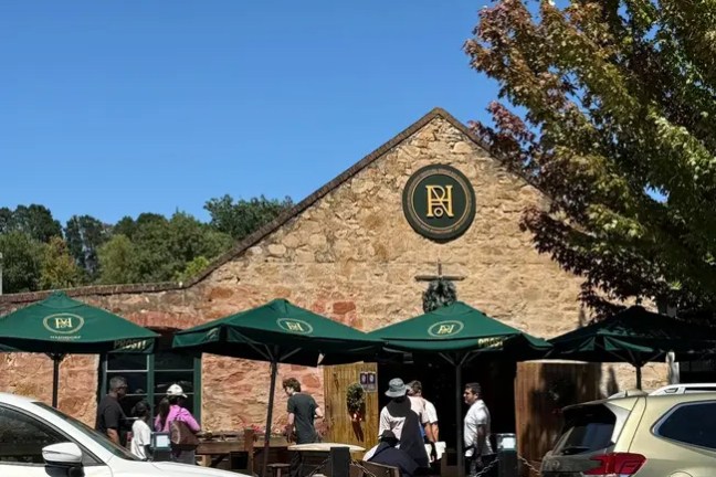 People outside a stone building with green umbrellas under a clear blue sky.