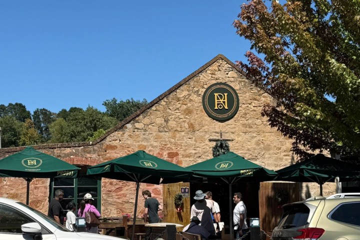 People sitting outside a brick café with a green logo under a clear blue sky.